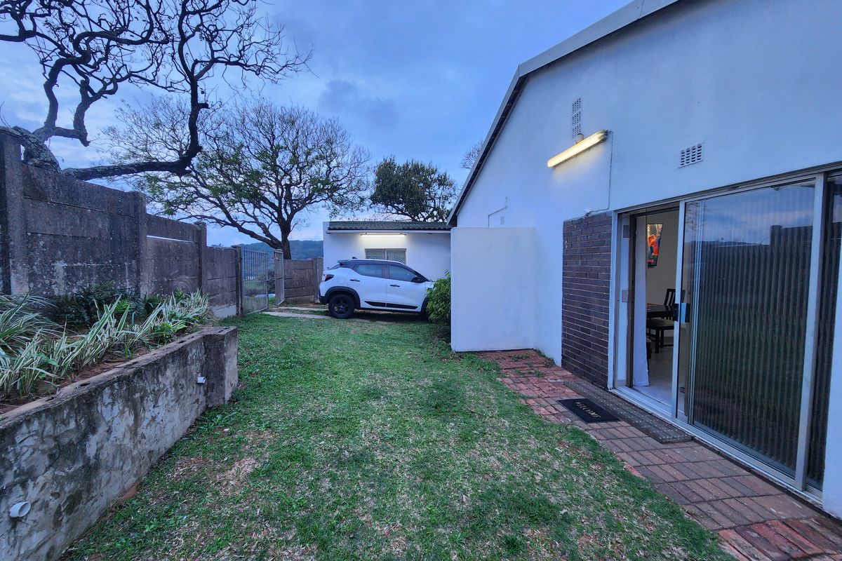 Rear exterior view showing a small lawn area, brick paving, sliding door access, and a concrete retaining wall.