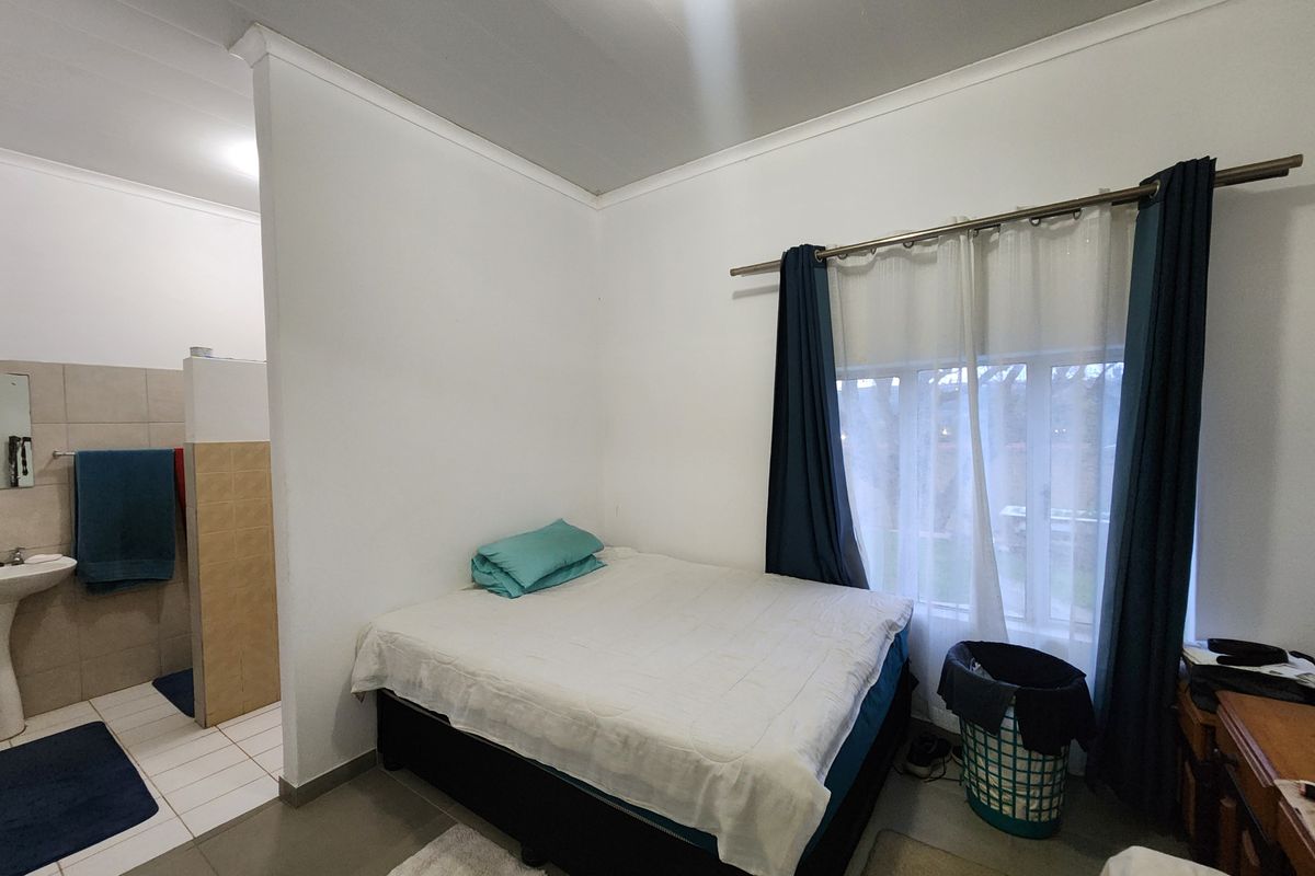 A bedroom featuring an open-plan en-suite bathroom with a pedestal basin and tiled flooring, offering a functional layout.