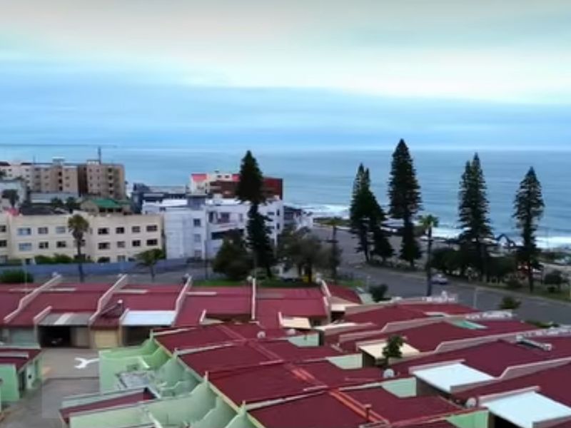 An elevated aerial view showing the townhouse complex rooftops with a scenic coastal and ocean backdrop.