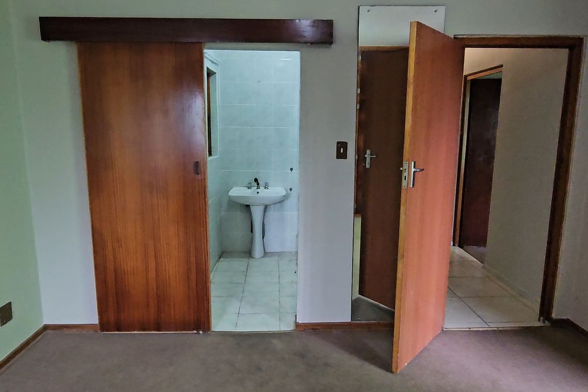 An empty bedroom featuring carpeted flooring, a sliding door leading to an en-suite bathroom with a pedestal basin, and a secondary doorway.