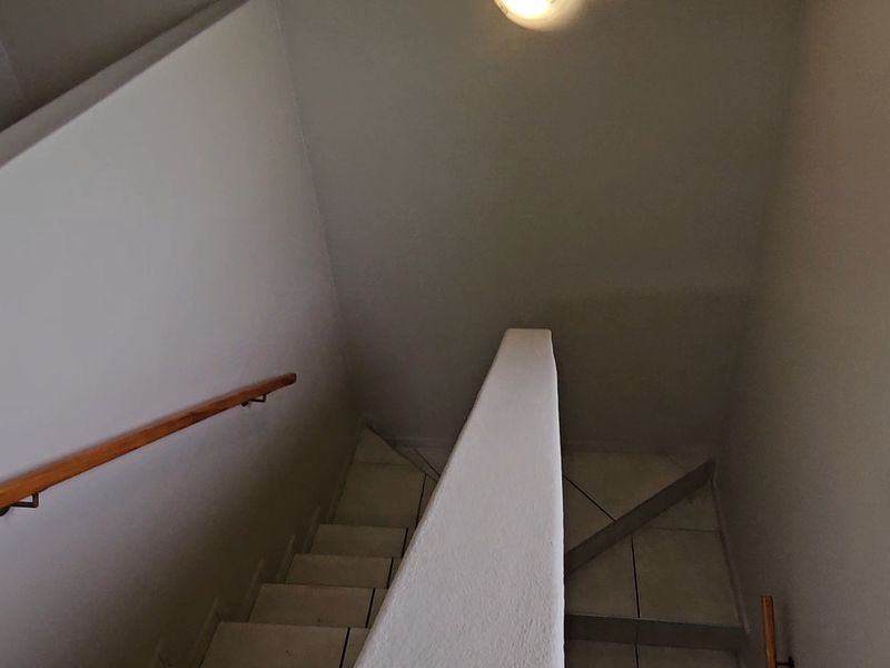 A functional staircase area featuring tiled steps, a wooden handrail, and a window with security bars, providing access between levels.