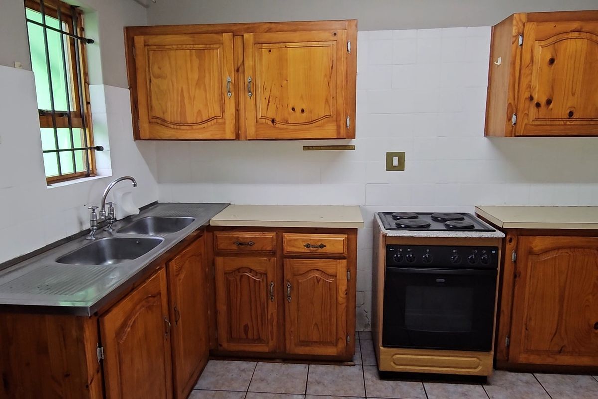 A functional kitchen featuring wooden cabinetry, a stainless steel double sink, and a freestanding electric stove with tiled splashbacks.