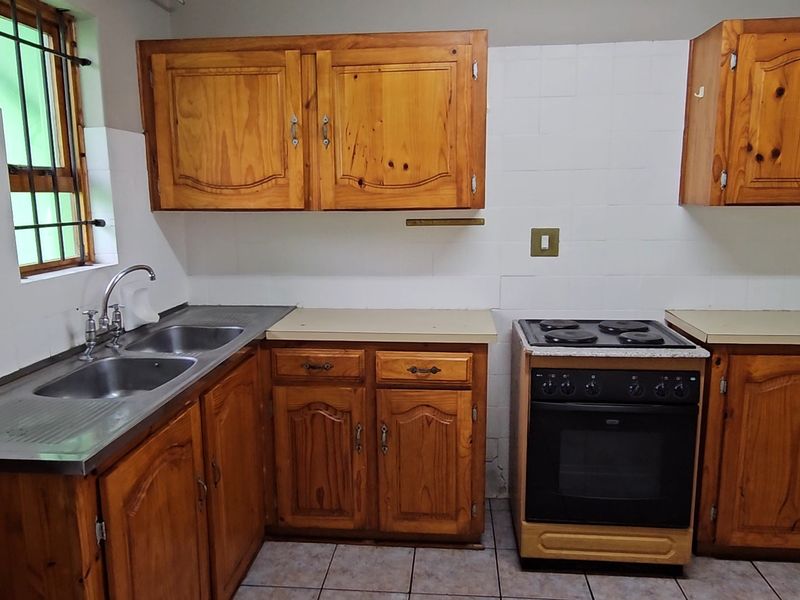 A functional kitchen featuring wooden cabinetry, a stainless steel double sink, and a freestanding electric stove with tiled splashbacks.
