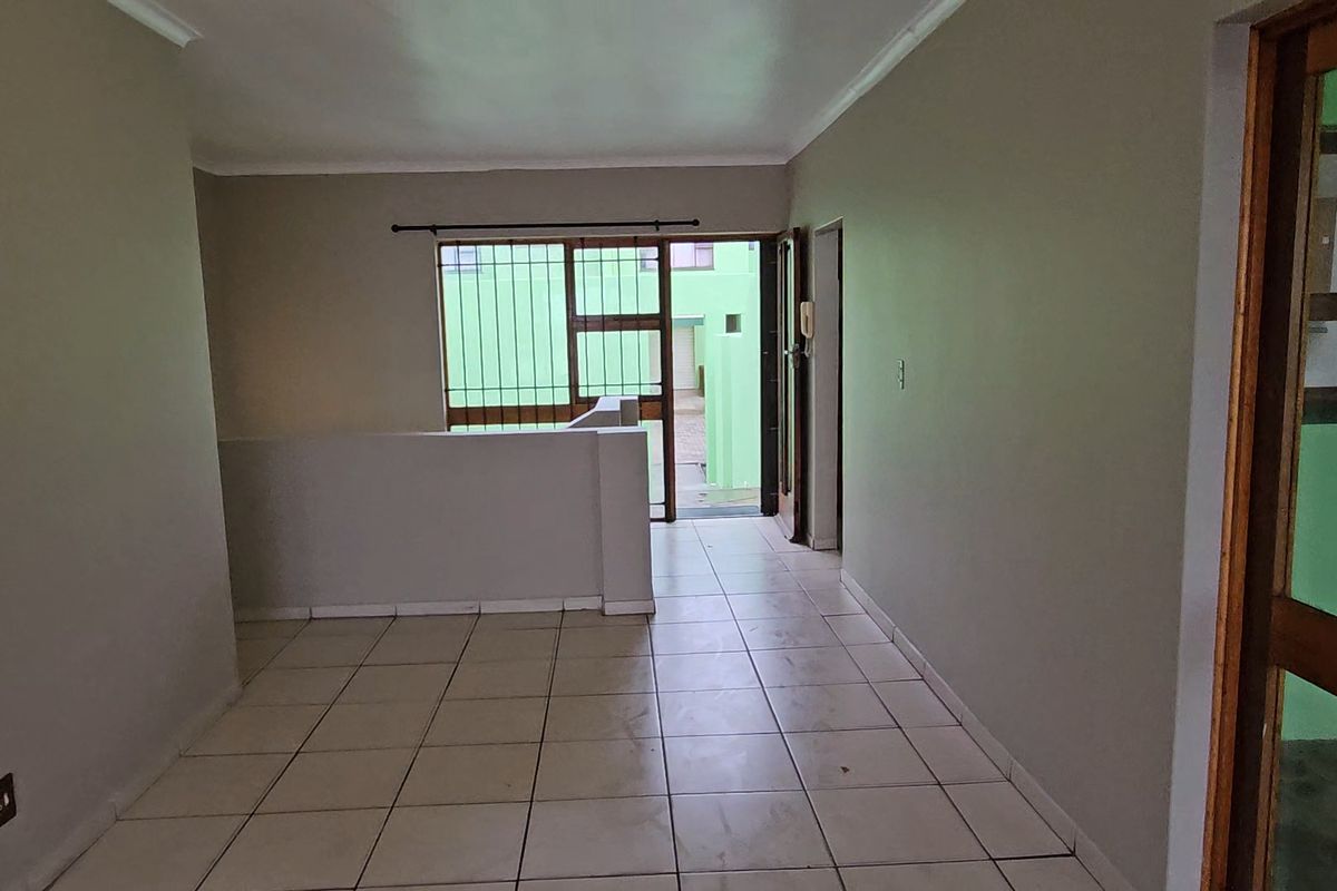 An empty, open-plan living area featuring tiled flooring, neutral walls, and direct access to an outdoor space through a sliding security door.