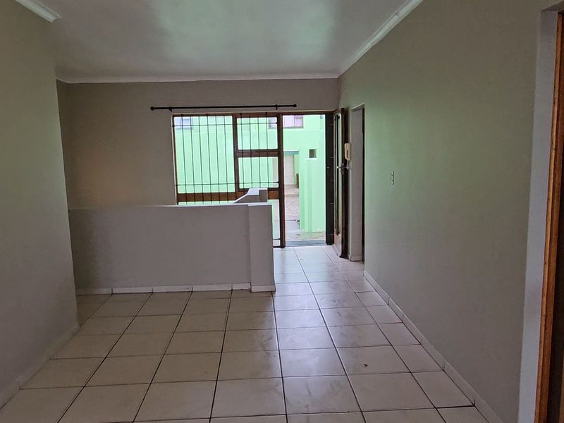 An empty, open-plan living area featuring tiled flooring, neutral walls, and direct access to an outdoor space through a sliding security door.