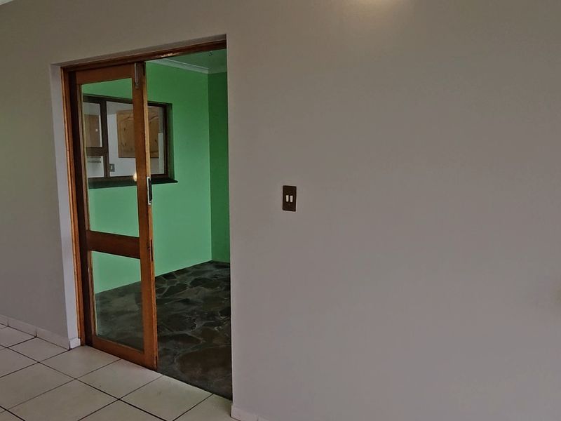 A spacious hallway featuring neutral wall tones, tiled flooring, and a wooden sliding door leading into an adjacent room with stone flooring.