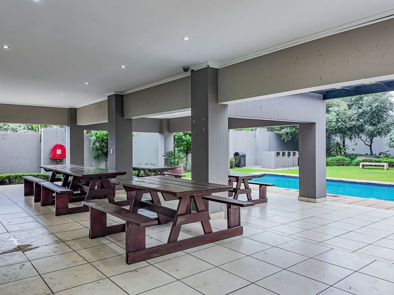 A covered outdoor entertainment area featuring tiled flooring, recessed lighting, and direct access to a swimming pool and garden space.