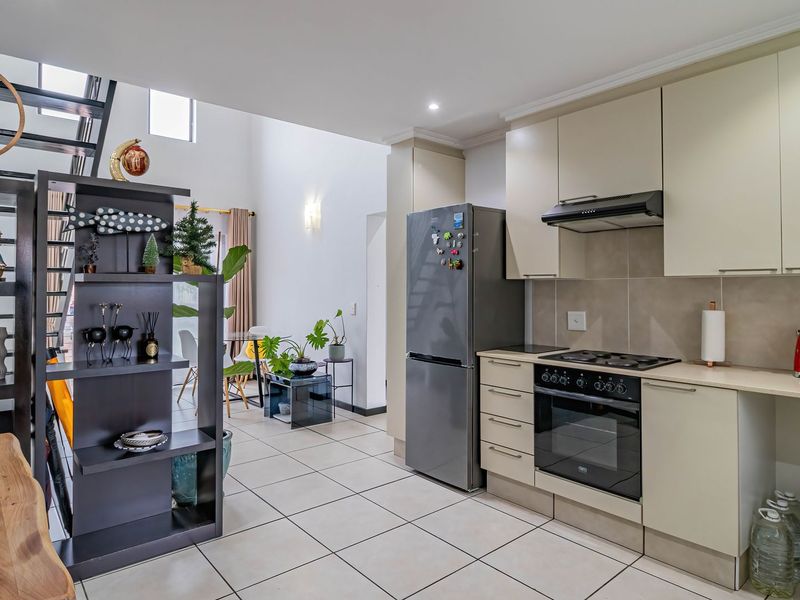 An open-plan kitchen and living area featuring modern cabinetry, built-in appliances, tiled flooring, and a staircase leading to an upper level.