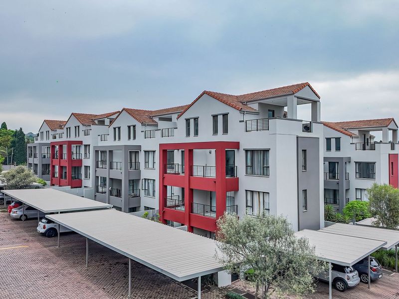 An aerial view of a modern apartment complex featuring multi-story units with balconies, tiled roofs, and covered carport parking areas.