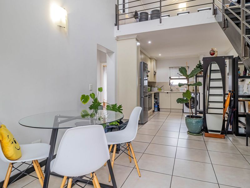 Open-plan living and kitchen area featuring a modern staircase leading to a mezzanine level, tiled floors, and functional built-in cabinetry.
