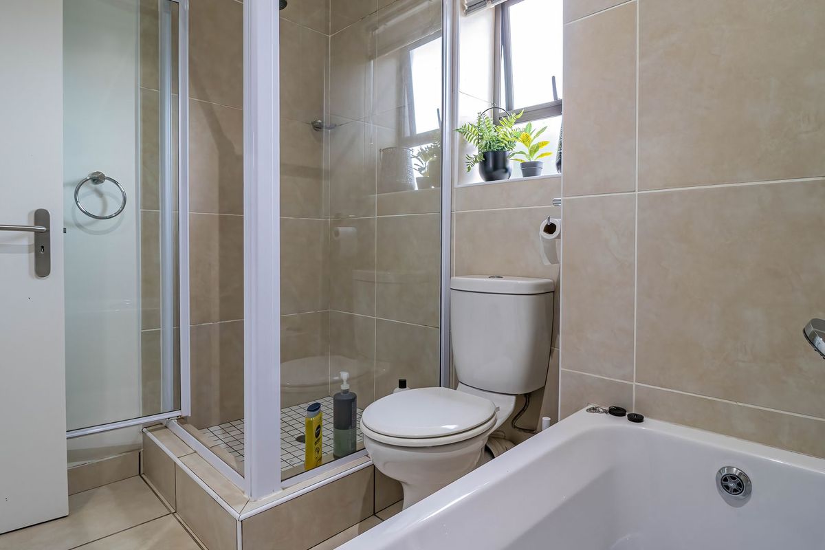 A functional bathroom featuring a glass-enclosed shower, a bathtub with mixer, and neutral wall tiling.