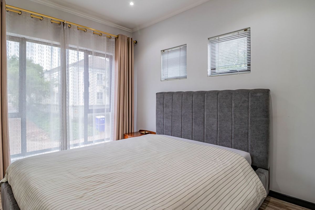 A well-maintained bedroom featuring laminate flooring, recessed lighting, and large sliding glass doors with integrated blinds, offering a bright and comfortable living space.