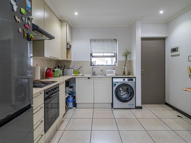 A functional kitchen featuring built-in cabinetry, laminate countertops, a stainless steel sink, integrated oven and hob, and tiled flooring with recessed lighting.
