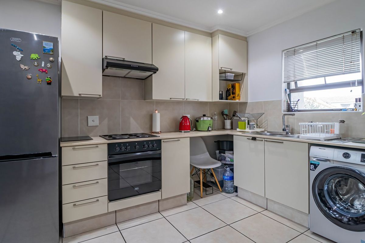A functional kitchen featuring neutral cabinetry, tiled backsplash, built-in oven with hob, extractor fan, and integrated space for laundry appliances.