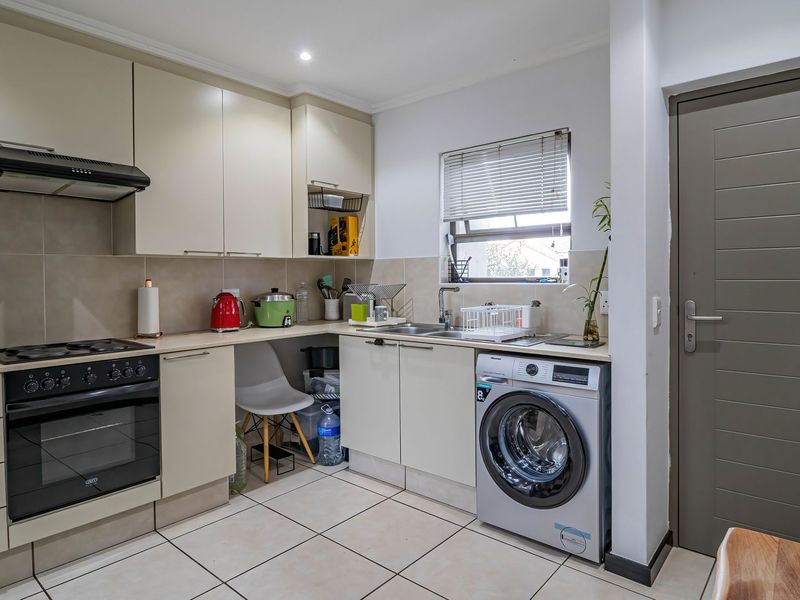 Functional kitchen featuring neutral cabinetry, built-in oven and hob, tiled backsplash, and integrated laundry plumbing, offering a practical layout for daily use.