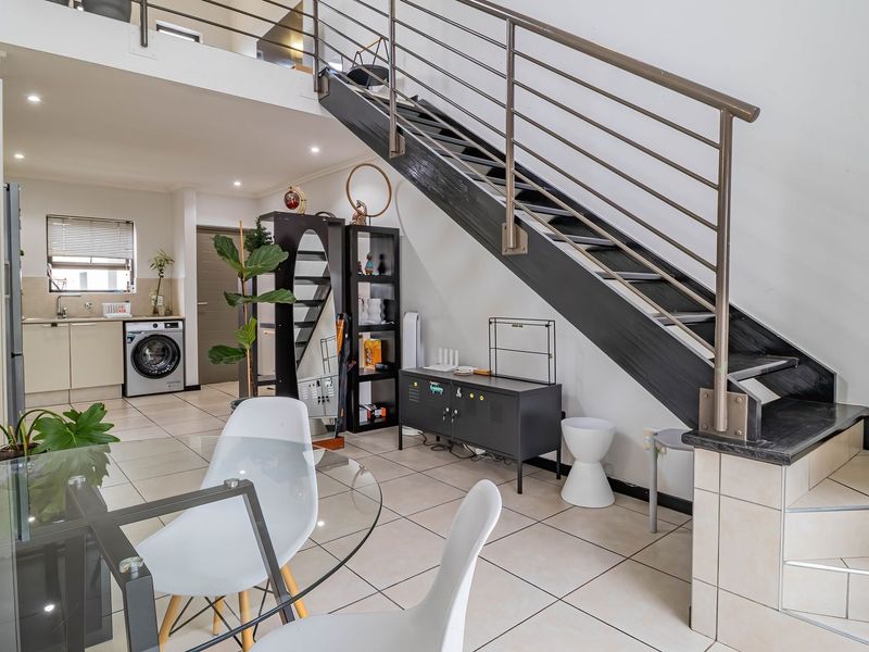 Open plan living area featuring a modern staircase with metal balustrade, tiled flooring, and a functional kitchen space with integrated laundry facilities.