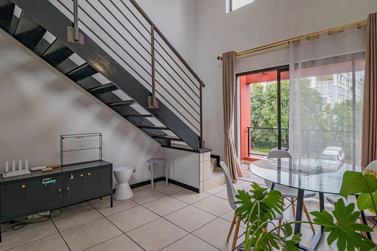 Bright living area featuring a modern metal staircase, tiled flooring, and direct access to a private balcony through sliding glass doors.