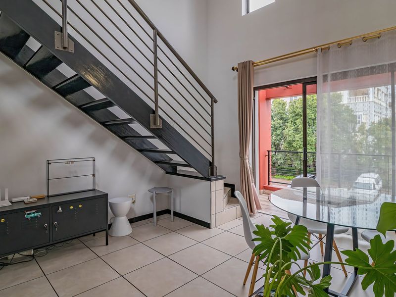 Bright living area featuring a modern metal staircase, tiled flooring, and direct access to a private balcony through sliding glass doors.