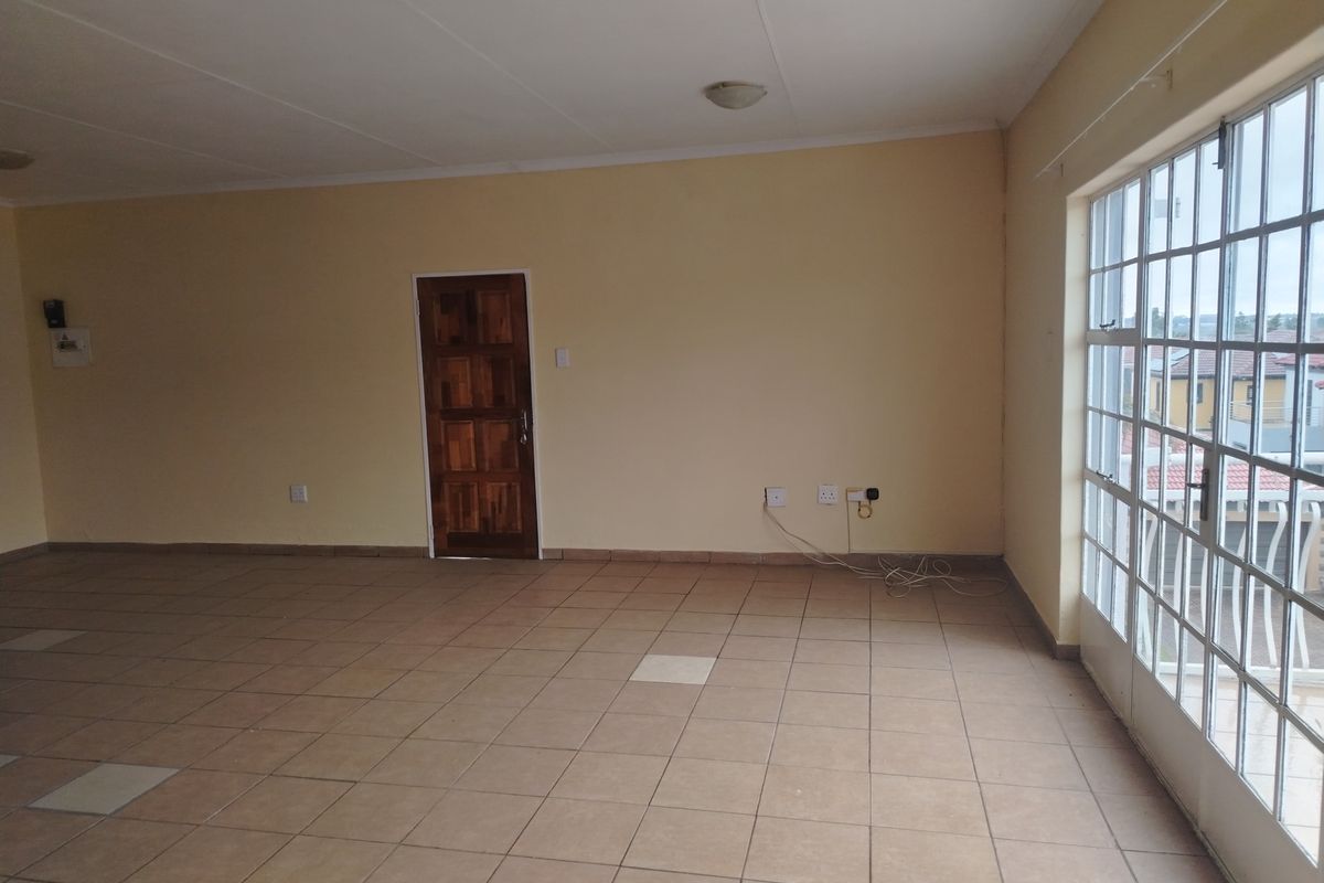 A spacious, empty living area featuring neutral walls, tiled flooring, and a large steel-framed window providing natural light.