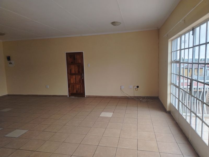 A spacious, empty living area featuring neutral walls, tiled flooring, and a large steel-framed window providing natural light.