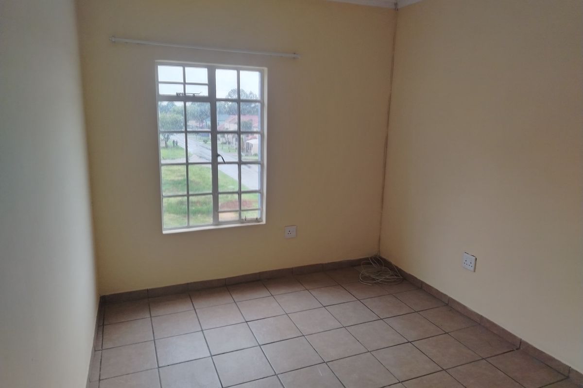 An empty bedroom featuring tiled flooring, a window with security bars, and neutral wall paint, providing a blank canvas for personalization.