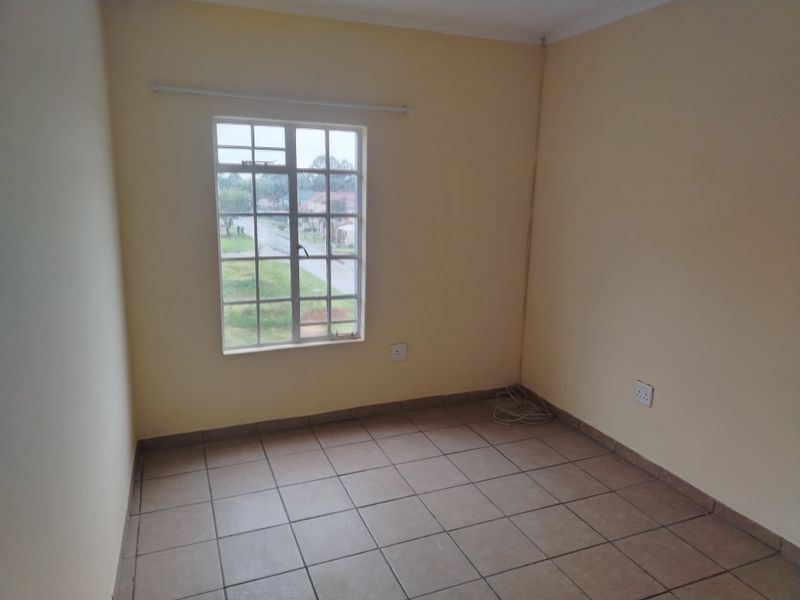 An empty bedroom featuring tiled flooring, a window with security bars, and neutral wall paint, providing a blank canvas for personalization.
