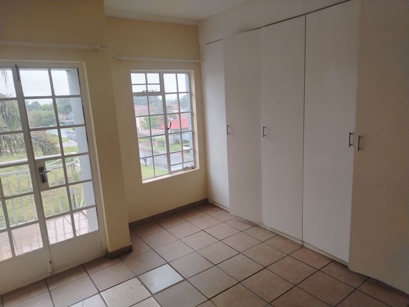 An empty bedroom featuring tiled flooring, built-in cupboards, and a glass-paneled door leading to a balcony.
