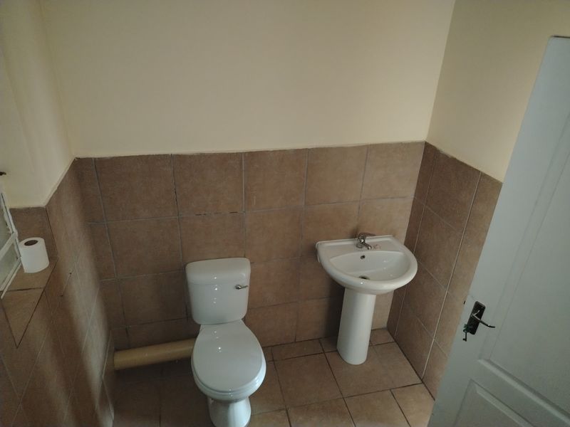 A compact bathroom featuring a pedestal washbasin, a standard toilet, and neutral ceramic wall and floor tiling.