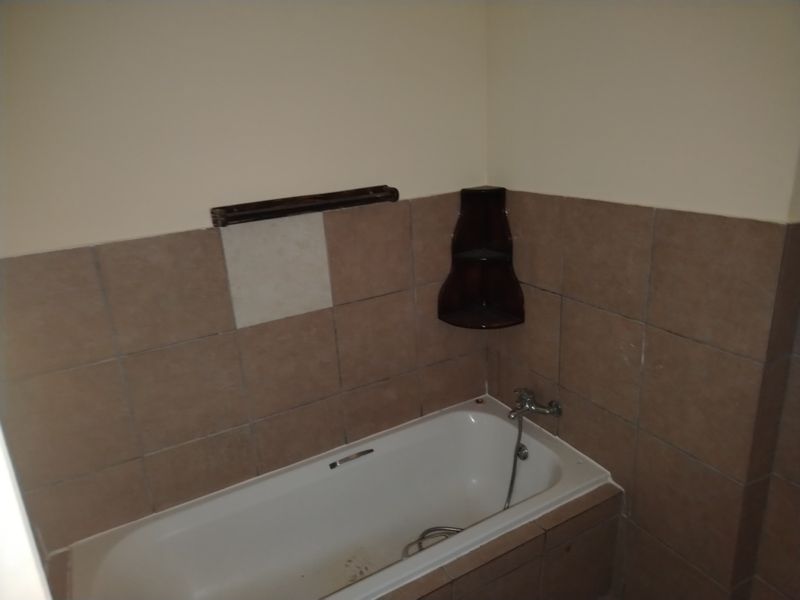 A bathroom featuring a built-in bathtub with tiled surround, handheld shower fixture, and corner shelving. The space requires minor repairs and cosmetic updates.