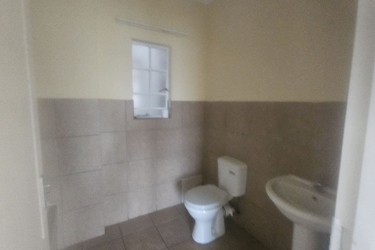 A functional bathroom featuring a pedestal washbasin, toilet, and neutral tiled finishes, providing a clean and simple space.