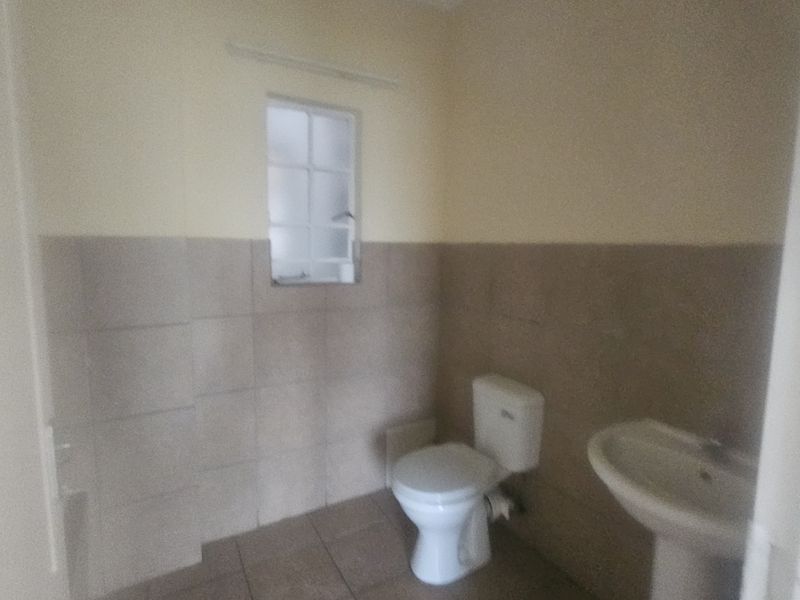 A functional bathroom featuring a pedestal washbasin, toilet, and neutral tiled finishes, providing a clean and simple space.