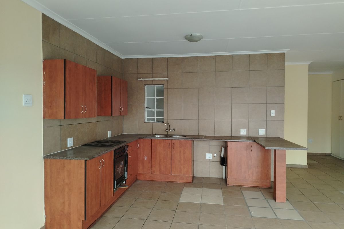 A functional kitchen featuring wood-look cabinetry, tiled backsplash, built-in oven and hob, and a breakfast bar extension, offering a clean, blank canvas for updates.