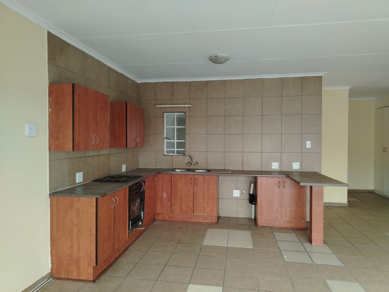 A functional kitchen featuring wood-look cabinetry, tiled backsplash, built-in oven and hob, and a breakfast bar extension, offering a clean, blank canvas for updates.