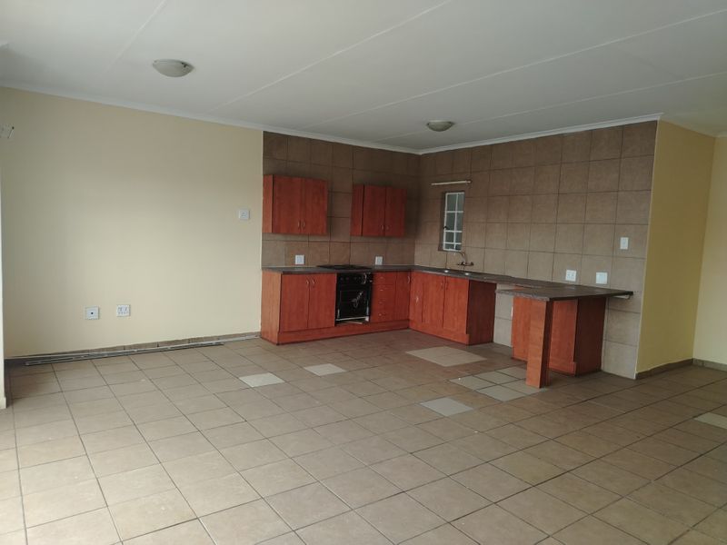 Open-plan kitchen and living area featuring built-in wooden cabinetry, tiled flooring, and a breakfast counter, presenting a blank canvas for customization.