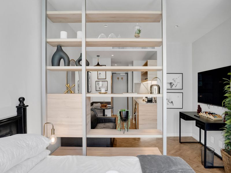 Modern open-plan apartment interior featuring a stylish timber room divider, herringbone flooring, and integrated lighting, creating a seamless flow between living and sleeping areas.