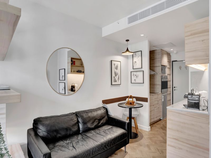 Modern open-plan living area featuring herringbone timber flooring, sleek built-in cabinetry, integrated kitchen appliances, and ducted air conditioning in a well-maintained apartment.