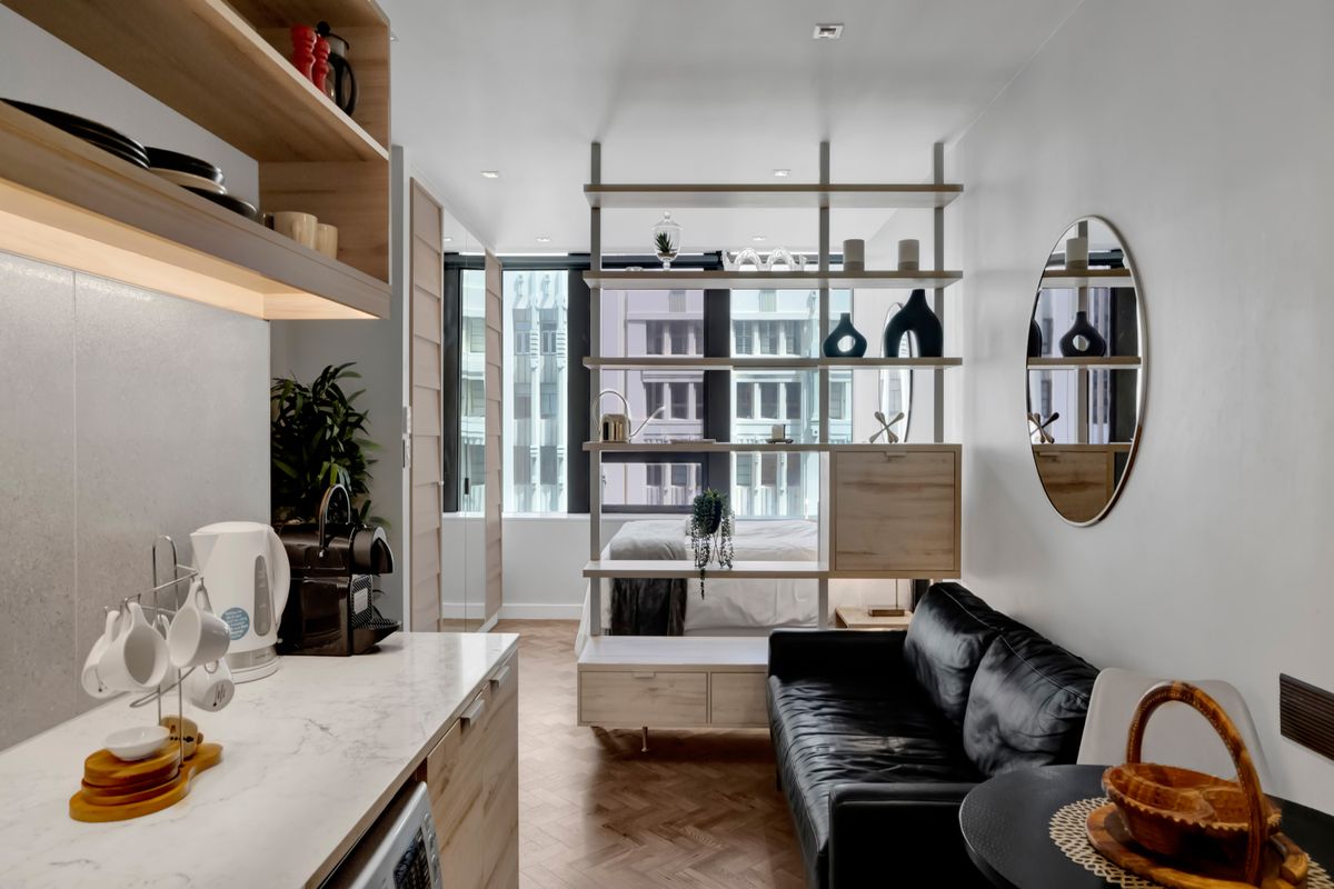 Modern open-plan studio apartment featuring herringbone timber flooring, a sleek kitchen with stone countertops, and a functional built-in room divider.