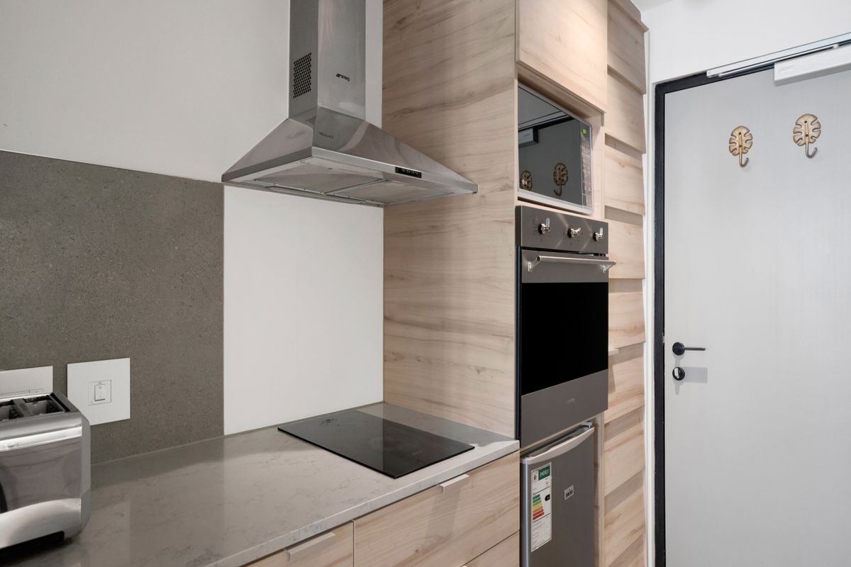 Modern kitchen featuring light wood-grain cabinetry, stone countertops, integrated oven, microwave, and stainless steel extractor fan.