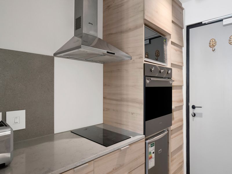 Modern kitchen featuring light wood-grain cabinetry, stone countertops, integrated oven, microwave, and stainless steel extractor fan.