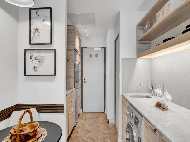 A compact, modern scullery or laundry area featuring stone countertops, integrated appliances, herringbone timber flooring, and custom cabinetry with integrated lighting.