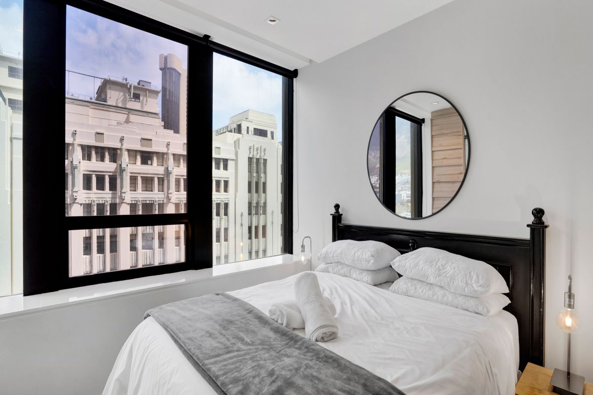 A bright and modern bedroom featuring large floor-to-ceiling windows that offer an urban city view and provide ample natural light.