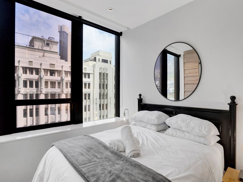 A bright and modern bedroom featuring large floor-to-ceiling windows that offer an urban city view and provide ample natural light.
