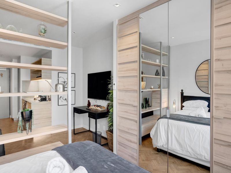 Modern open-plan apartment featuring high-quality finishes, herringbone timber flooring, integrated shelving, and mirrored wardrobe doors, creating a seamless and functional living space.