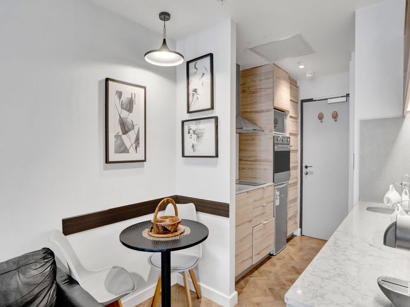 Modern open-plan apartment featuring a compact kitchen with integrated appliances, stone countertops, and elegant herringbone timber flooring.