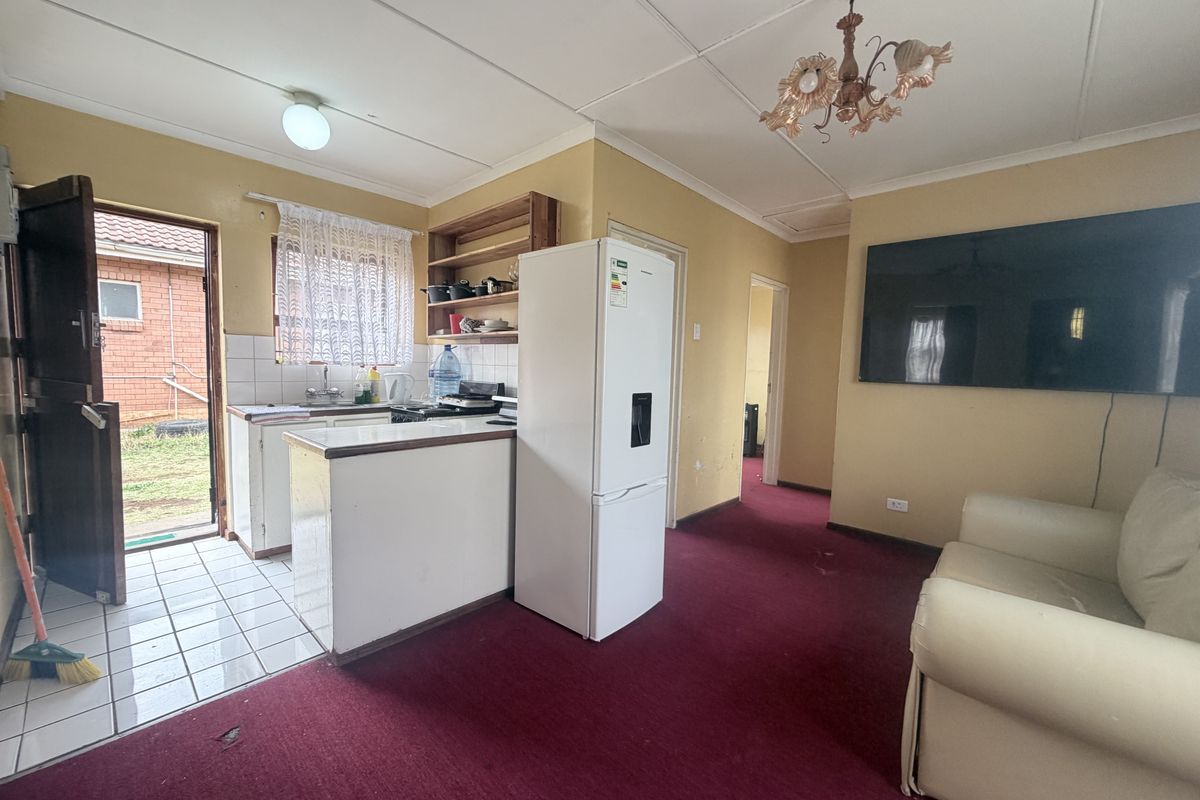 Open-plan living and kitchen area featuring a compact kitchenette, tiled entrance, and carpeted living space, offering potential for modernization and layout optimization.