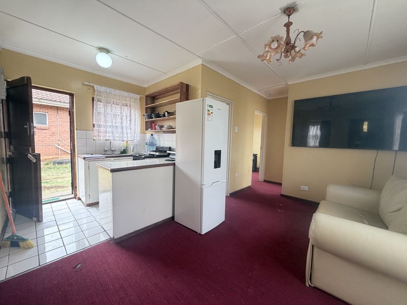 Open-plan living and kitchen area featuring a compact kitchenette, tiled entrance, and carpeted living space, offering potential for modernization and layout optimization.
