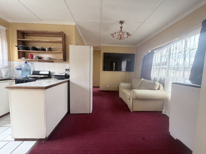 Open-plan living and kitchen area featuring a breakfast counter, tiled kitchen flooring, and carpeted living space with security-barred windows.