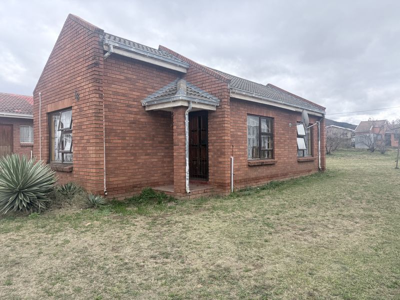 A single-story face brick house featuring a tiled roof, security gate, and aluminium window frames, set on a grassed plot.