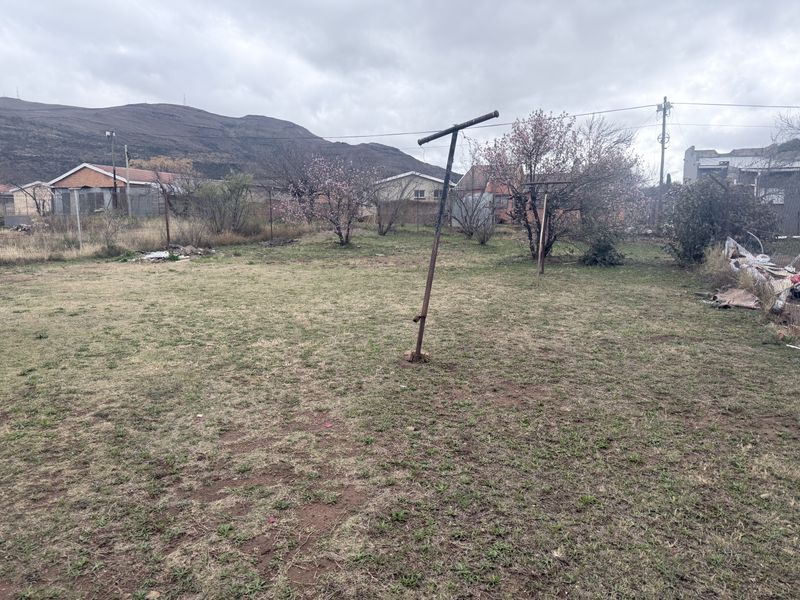 A spacious, open backyard area featuring a metal washing line pole and perimeter wire fencing, set against a mountainous backdrop.