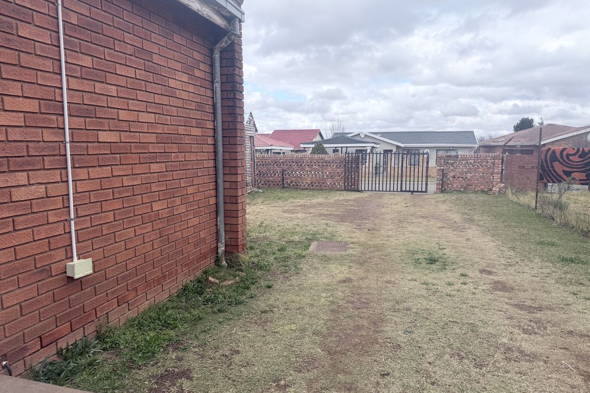 A view of the rear yard featuring a brick exterior wall, a metal gate, and a grassed area.